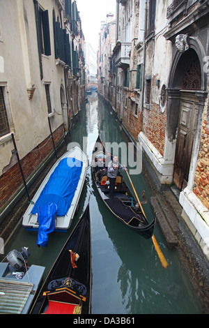 Gondolas and gondoliers on a small side Canal with colourful old buildings  Venice Italy in winter Stock Photo