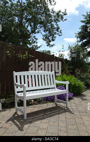 a white wooden bench in a garden setting Stock Photo