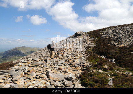 Man walker standing on the thick stone outer wall of Tre'r Ceiri iron Age Hill Fort Yr Efil The Rivals Llyn Peninsula Wales UK Stock Photo