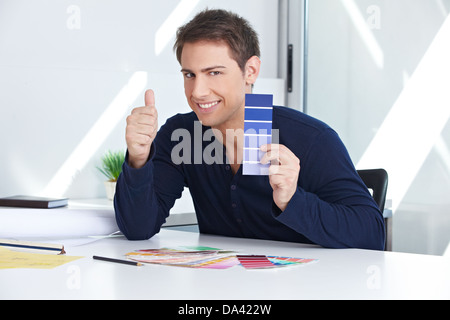 Designer with blue color samples at his desk in the office holding thumbs up Stock Photo