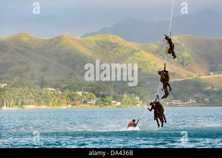 US Navy SEAL team members dangle from the Special Patrol Insertion and Extraction rope attached to an UH-60 Black Hawk helicopter during HELOCAST training at Marine Corps Air Station Kaneohe Bay June 19, 2013 in Hawaii. Stock Photo