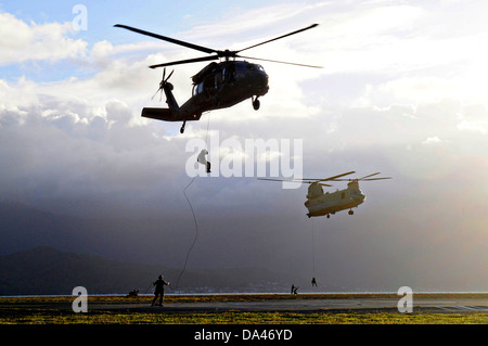 US Navy SEAL team members rappel from the Special Patrol Insertion and Extraction rope attached to an UH-60 Black Hawk helicopter and a CH-47F Chinook helicopter during HELOCAST training at Marine Corps Air Station Kaneohe Bay June 19, 2013 in Hawaii. Stock Photo