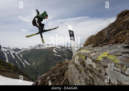 NUFENEN, VALAIS, SWITZERLAND. A freestyle freeskier is executing a trick on a handmade kicker to jump over a road marker. Stock Photo