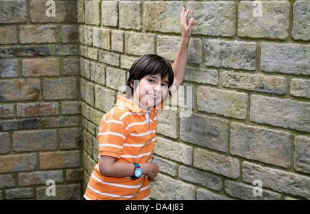 Portrait of smiling brunette boy leaning on stone wall with arms raised Stock Photo