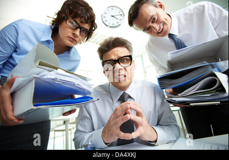 Pleading accountant looking at camera being surrounded by his partners holding huge piles of documents Stock Photo