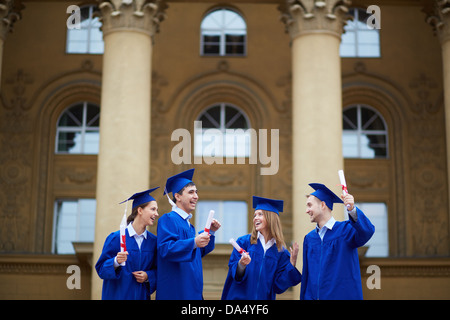 Group of joyful students in graduation gowns holding diplomas Stock Photo