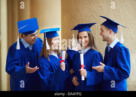 Group of smart students in graduation gowns having chat Stock Photo
