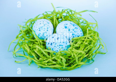 Three blue speckled easter eggs in green paper grass nest Stock Photo