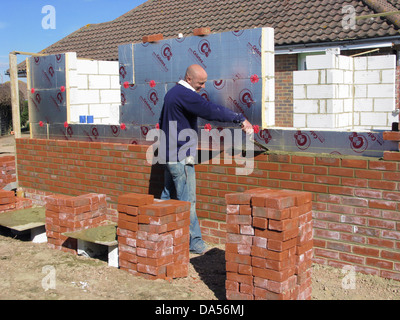 Builder cementing & building a brick wall with celotex thermal insulation board & cavity walls in an extension or new property Stock Photo
