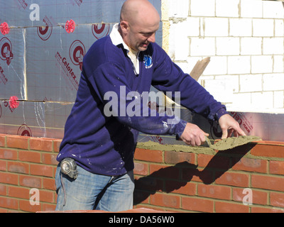 Builder cementing & building a brick wall with celotex thermal insulation board & cavity walls in an extension or new property Stock Photo