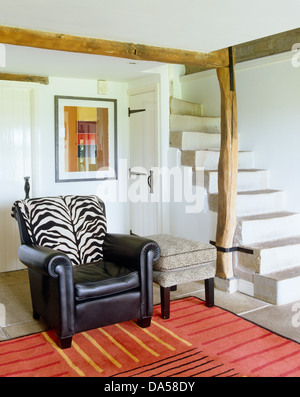 Zebra print cushion on black leather armchair in contemporary cottage hall with red rug and stone stairs Stock Photo