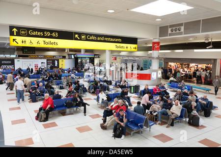 Travellers waiting in Gatwick airport departure lounge below direction signs. Stock Photo