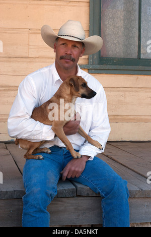 Cowboy holding his Jack Russell Terrier, sitting on the porch of an old west building Stock Photo