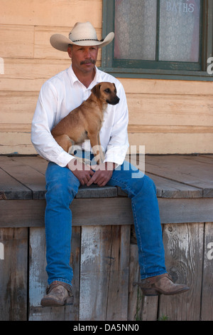 Cowboy holding his Jack Russell Terrier, sitting on the porch of an old west building Stock Photo