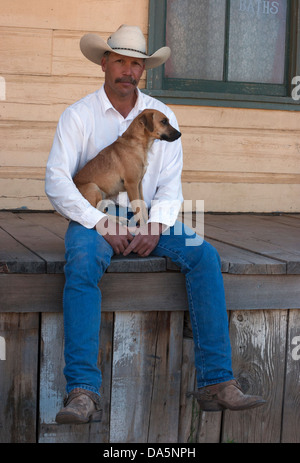 Cowboy holding his Jack Russell Terrier, sitting on the porch of an old west building Stock Photo