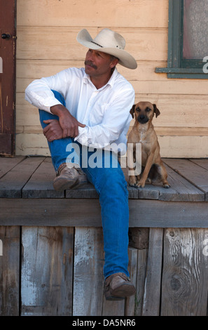 Cowboy with his dog, sitting on the porch of an old west building Stock Photo