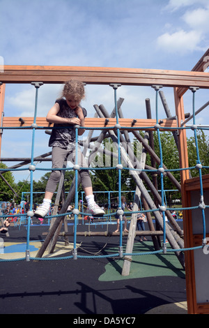 A five year old girl climbs across a rope section of a climbing frame in an adventure playground in an urban park Stock Photo