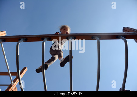 A five year old girl climbs balances monkey bars Stock Photo