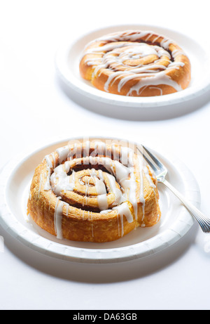 Two fresh hot cinnamon rolls on white plates in window light Stock Photo