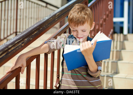Young happy kid reading book on school stairs Stock Photo