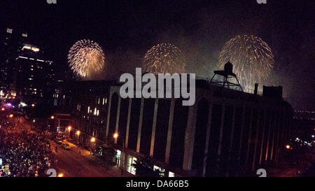 New York, USA. 04th July, 2013. Crowds on 11th Avenue watch Macy's spectacular annual fourth of July 04 4th patriotic holiday fireworks firework display lights light up the sky above Hudson River beyond city skyline of Hells Kitchen neighborhood & silhouetted form of old wooden water tower watertower Credit:  Dorothy Alexander/Alamy Live News Stock Photo