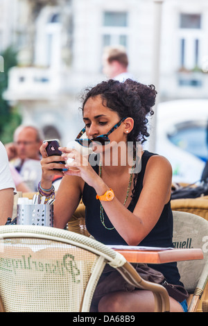 An attractive young woman uses her iPhone whilst seated at an outdoor cafe in Old Town Square, Prague Stock Photo
