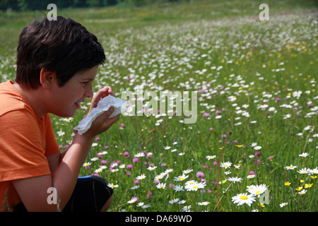 allergic child to pollen and flowers with a handkerchief while sneeze in the middle of meadow Stock Photo