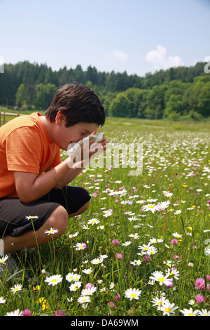 child with an allergy to pollen while sneeze in the middle of the flowers Stock Photo