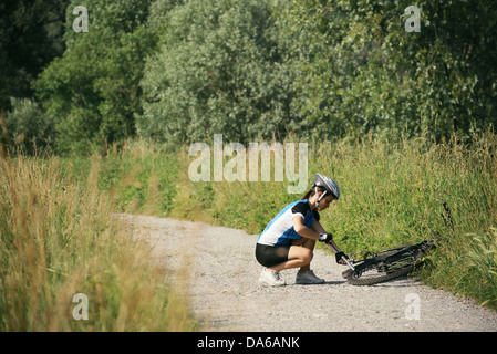 young woman training on mountain bike and repairing flat tyre on track in countryside Stock Photo