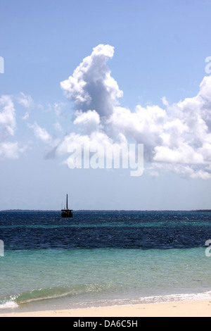 A traditional dhow sail boat on emerald blue water alongside a sandy white beach in Zanzibar Stock Photo