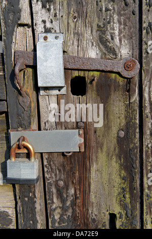 Close up of an old padlock and a rusty latch on a distressed barn door. Stock Photo