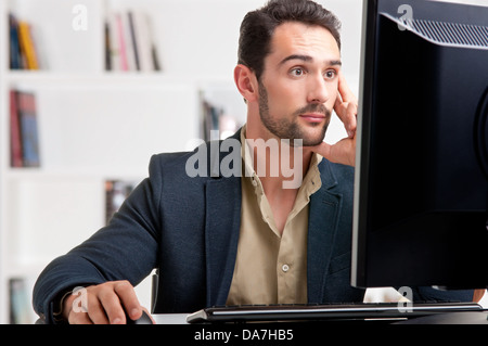 Surprised man looking at a computer screen, thinking about the job at hand Stock Photo