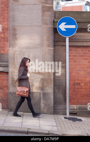 Young woman walking in the opposite direction pointed to by a one way traffic road sign Stock Photo