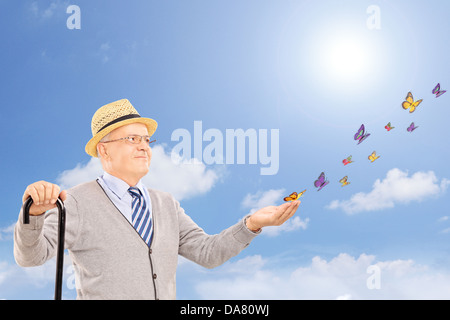 Mature smiling man holding a cane and looking at colorful butterflies Stock Photo