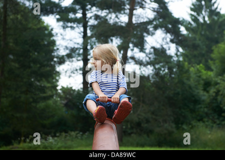 Child blond girl having fun on the seesaw at a park summer Stock Photo