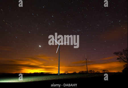 Two wind turbines pictured at sunrise with star trails Stock Photo