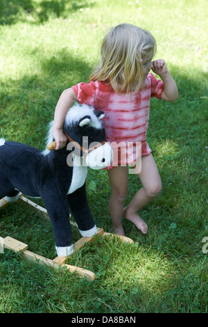 Child blond girl on a rocking horse outside, summer garden Stock Photo