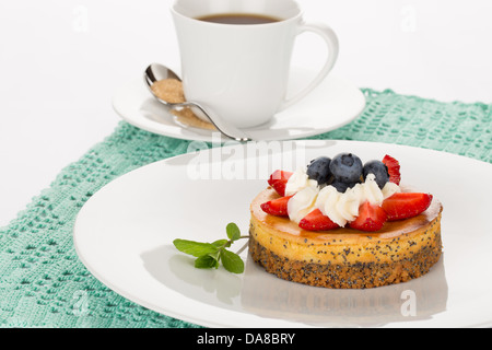 Cheesecake with strawberry, blueberry, mint and cream on white plate with cup of tea. Stock Photo