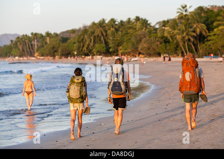 Backpackers walk along the beach wearing a rucsac in Playa Tamarindo Guanacaste Costa Rica Stock Photo