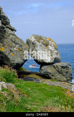 Tourist boat seen through rocks on the coast path in Cornwall close to St Ives Stock Photo