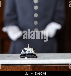Concierge with white gloves pointing to hotel bell on counter Stock Photo