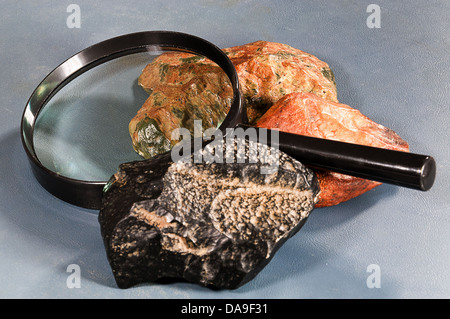 Samples of black and green nephrite jade as they are found in nature with an apple green specimen under a magnifying glass. Stock Photo