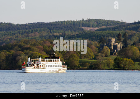 A view of a white passenger vessel on Windermere with Wray castle in the distance on a sunny afternoon. Stock Photo