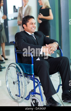 cheerful Indian businessman in wheelchair with colleagues on background Stock Photo