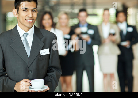 smiling young Indian businessman having coffee break during seminar Stock Photo