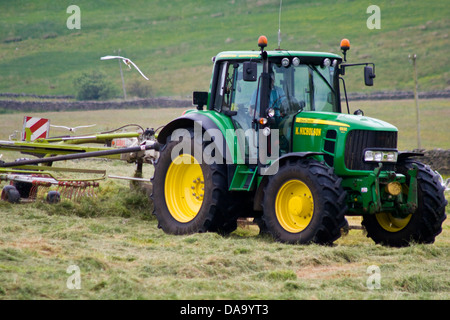 A tractor rows up grass at silage time on an upland farm Stock Photo