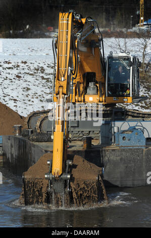 An excavator on a platform clears the Main Danube Canal from stones in Hausen, Germany, 22 January 2011. The canal was first covered with ice, then flooded and now it is filled with tons of stones. Therefore, it remains closed in the section between Bamberg and the sluce Hausen nearby Forchheim. Ships will be allowed to pass as early as the beginning of February. Photo: David Ebene Stock Photo