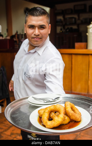 Waiter carrying tray of picarones dessert donuts in at El Bolivariano barbecue restaurant cafe diner cuisine, Lima, Peru. Stock Photo