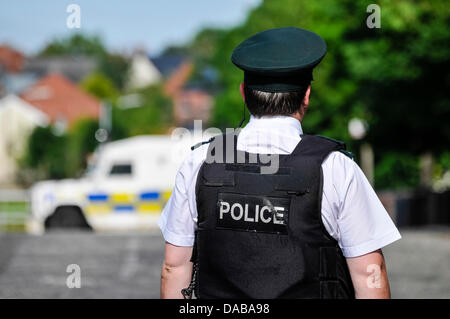 A PSNI Police Officer looks towards an armoured Landrover parked in the middle of a road Stock Photo