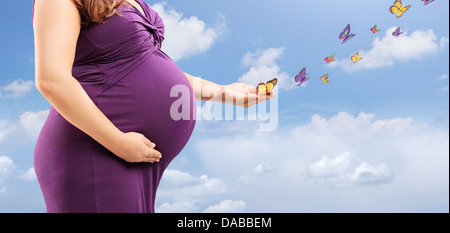 Pregnant woman holding her belly and butterflies on her hand Stock Photo